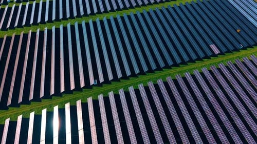 Multiple photovoltaic cells producing green energy. Drone footage over the rows of solar panels.