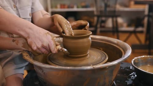 Focuced close up view. Using the pottery wheel to shape the clay. Mother is with little girl