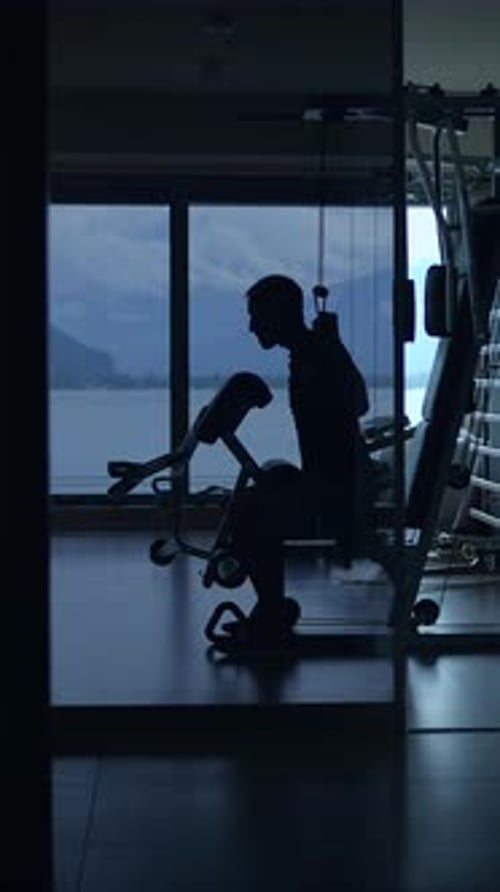 A Silhouetted Individual is Actively Exercising in a Modern and Wellequipped Gym Environment