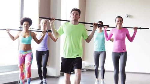 Diverse group training together doing squats with bars in a bright gym
