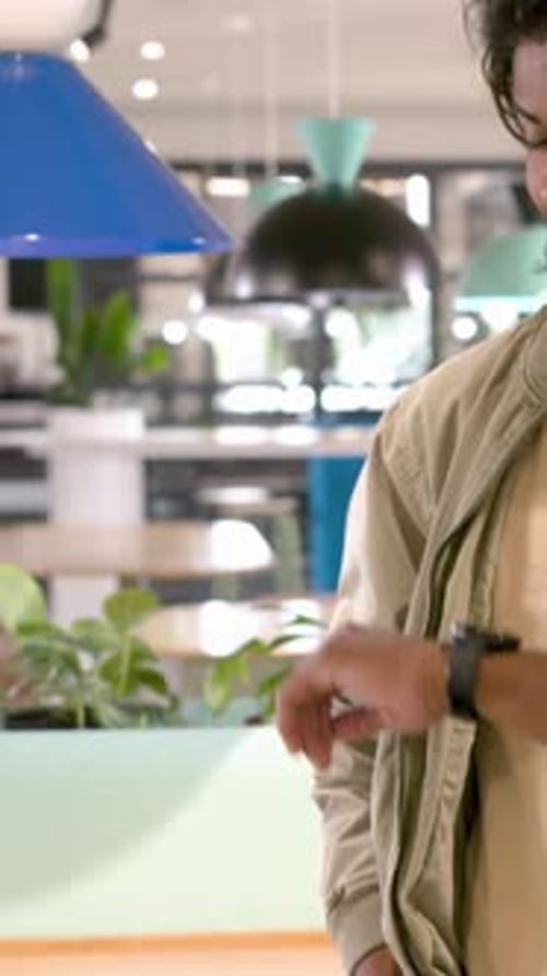 Vertical video: Framing khaki jacket man checking smartwatch, turning smiling at cafe, copy space