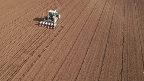 Aerial drone shot of a farmer in tractor seeding, sowing agricultural crops at field.