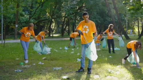 Group Of Multiethnic Eco Activists In TShirts With Recycling Symbol Cleaning Park People With