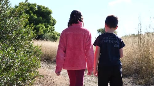 Young kids brother and sister walking together on a path. Slow-motion gimbal shot.