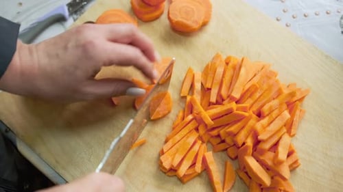 Close-up of woman hands cutting fresh carrots into sticks on kitchen board