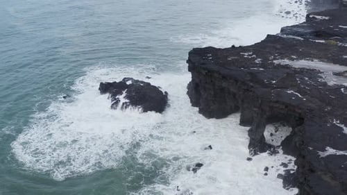 Aerial orbiting shot showing gigantic waves crashing against rocky basalt coastline of Iceland