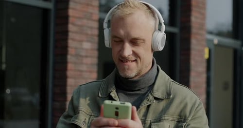 Man with Headphones Looking at Phone Smiling