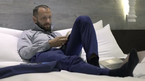 Young businessman enjoying a relaxing evening reading in a hotel bedroom
