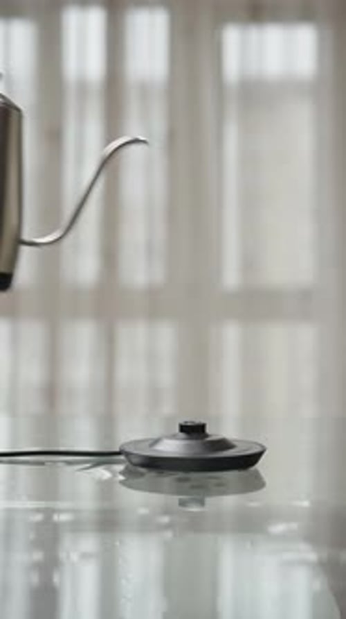 Vertical Cropped Shot of Man Putting Stainless Steel Electric Kettle on Charging Base on Background