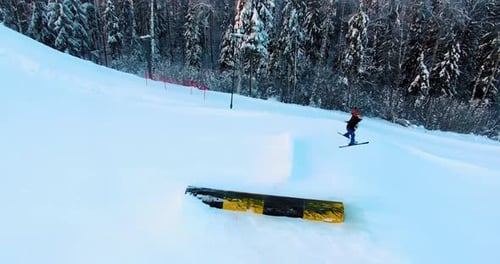 Side aerial view of a skier jumping off a slope in a terrain park.