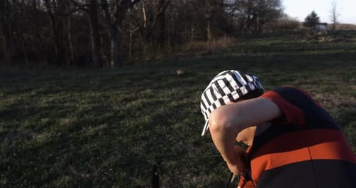 Young boy in striped cap practicing archery with bow in grassy field at sunset, Siloam Springs, Arka