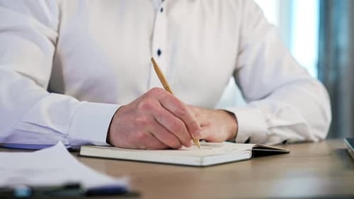 Man Writes Notes on a Notebook at Desk