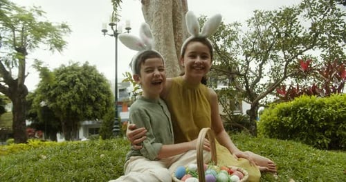Kinder mit Hasenohr-Stirnbändern auf dem Kopf sitzen zu Ostern auf einer Wiese und umarmen sich gegenseitig