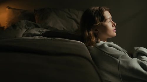 Fille mélancolique appuyée contre un lit sur le sol dans une chambre sombre