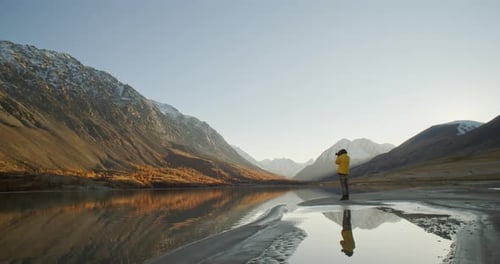 Traveler Taking Photo with Camera By Mountain Lake at Sunrise