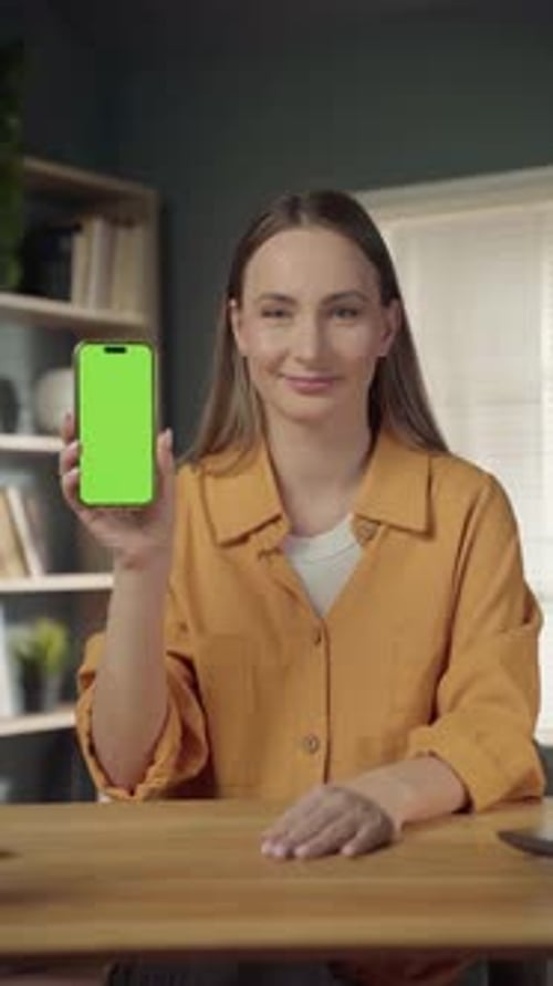 Smiling Young Woman Holds Smartphone with Blank Green Screen in Modern Home Office Ideal for App Ad