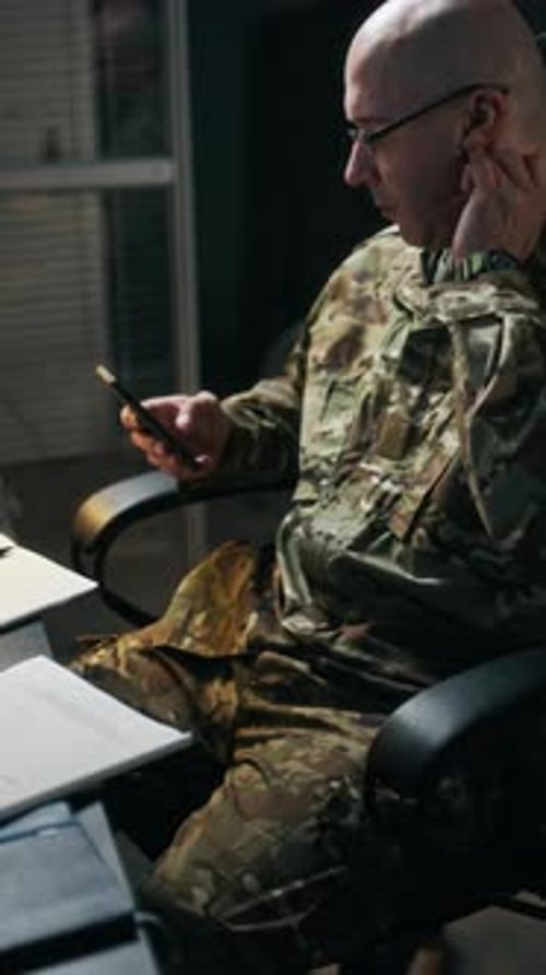 Man in Camouflage Using Phone at Desk Indoors