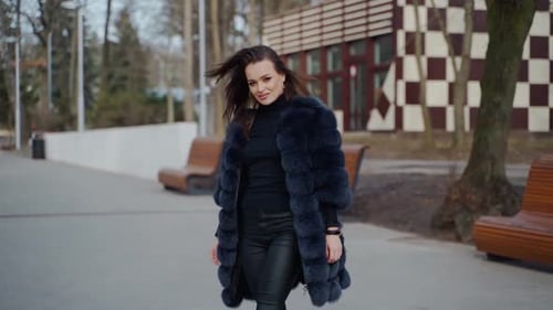 Attractive girl posing in the park. Beautiful young woman in black fur coat looking on camera