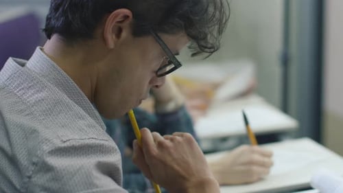 Vidéo d'un étudiant hispanique écrivant avec des lunettes dans une classe de collage pendant un cours.
