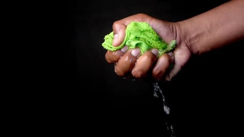 Slow Motion of Hands Squeeze Wet Towel Against Black Background Draining Water From Wet Towel