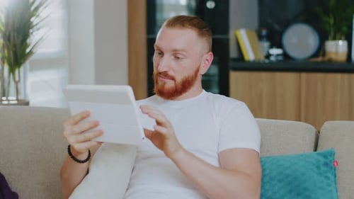 Man Relaxing on Sofa Uses Tablet at Home