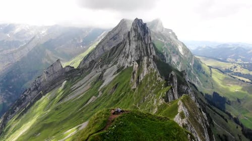 Aerial flyover over the two hikers enjoying the view of Schafler ridge in Appenzell, Switzerland wi
