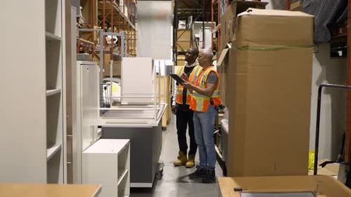 Warehouse supervisor training employee on digital tablet in shipping department