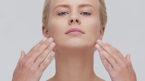 Studio Portrait of Young Beautiful and Natural Blond Woman Applying Skin Care Cream Face Lifting