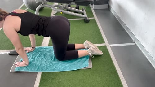 close view of Young woman kneels to perform an exercise to work her back in a gym.