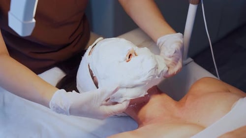 Full Alginate Mask Covers Caucasian Woman's Face During Clinic Facial Treatment Aesthetician in