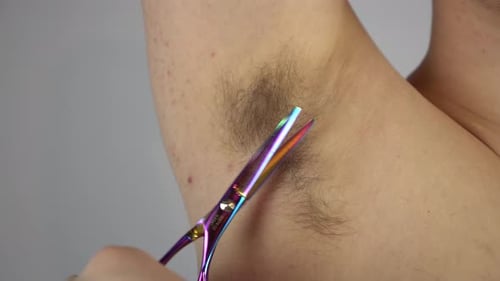 Un joven se corta el pelo largo en la axila con unas tijeras de peluquería