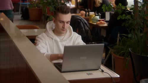 Arbeitsumgebung. Ein junger Mann sitzt im Café und arbeitet am Laptop, während er telefoniert
