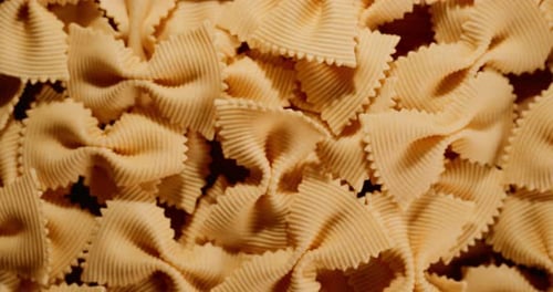 A pile of uncooked butterfly pasta on a wooden table (close-up shot tilting from top down to side)