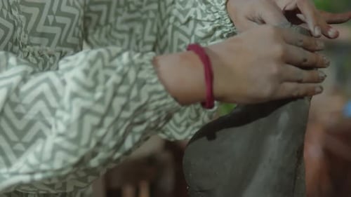A potter shapes clay with skilled hands in a close-up shot, emphasizing traditional craftsmanship