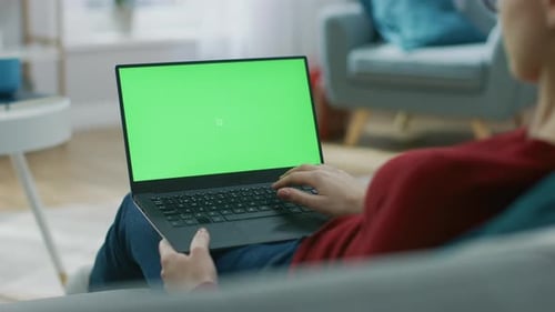 Young Woman at Home Sitting on a Couch Works on a Laptop Computer with Green Mock-up Screen. Girl U