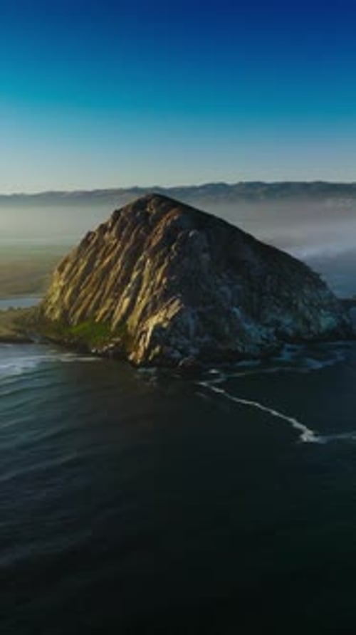 Magical sight of Morro Bay covered with thick fog. Triangle rock at the shore of Central coast