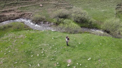 Adventurer Walking Through Grassy Field Near Stream