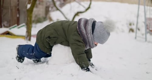 Child Building Snowball in Winter Garden