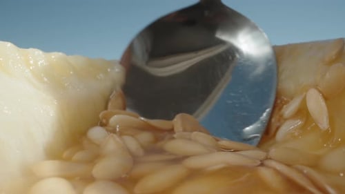 Eine halbe Melone, die Kerne darin mit einem Löffel herauskratzen. Sonne, blauer Himmel. Dolly Slider extreme Nahaufnahme.