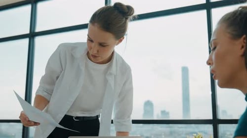Two Women Discuss Business Charts in Office Setting