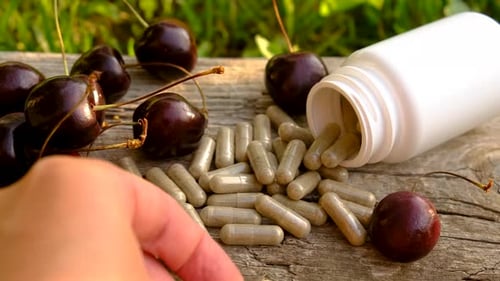 Cherries, Bottle, and Dietary Supplement Capsules on Wood