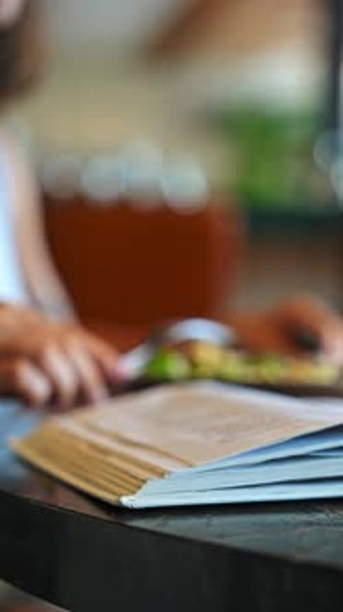 Vertical Shot of Female Hand Turning Page of Open Book on Wooden Table