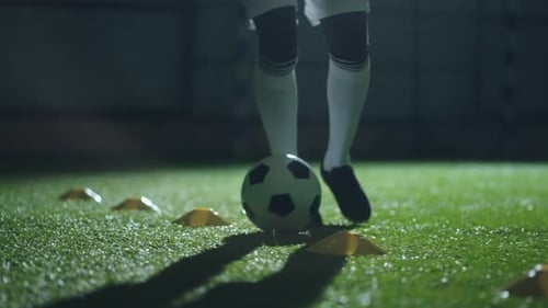 Dribbling Ball in Football Hall Closeup of Legs of Soccer Player Running Over Artificial Grass