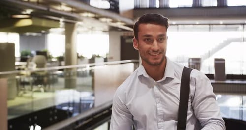 Smiling businessman in office building, carrying bag and looking down