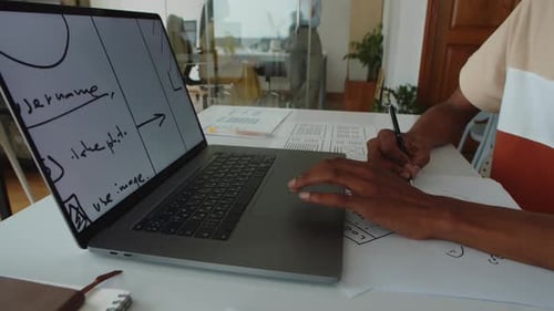 Designer Works with Laptop and Paperwork at Desk