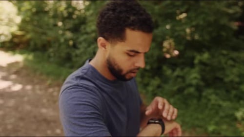 Young male stops to check smartwatch during run