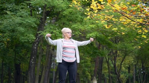 The senior active female does aerobics or gymnastics exercises in an outdoor park. A retired 50s