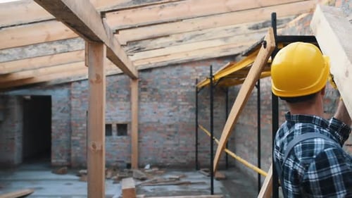 Walks with piece of board. Construction worker in uniform and safety equipment have job on building