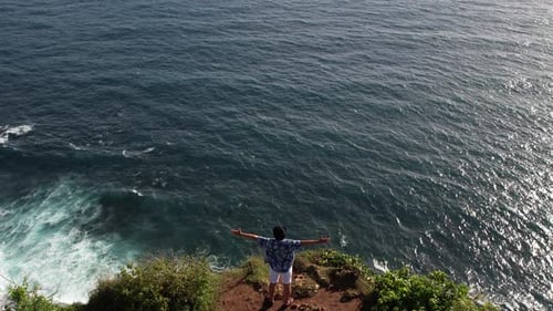 Man Stand on Edge of Cliff Spread Arms Wide and Looking Into the Endless Ocean