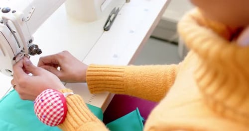 Biracial female fashion designer threading sewing machine in studio, slow motion